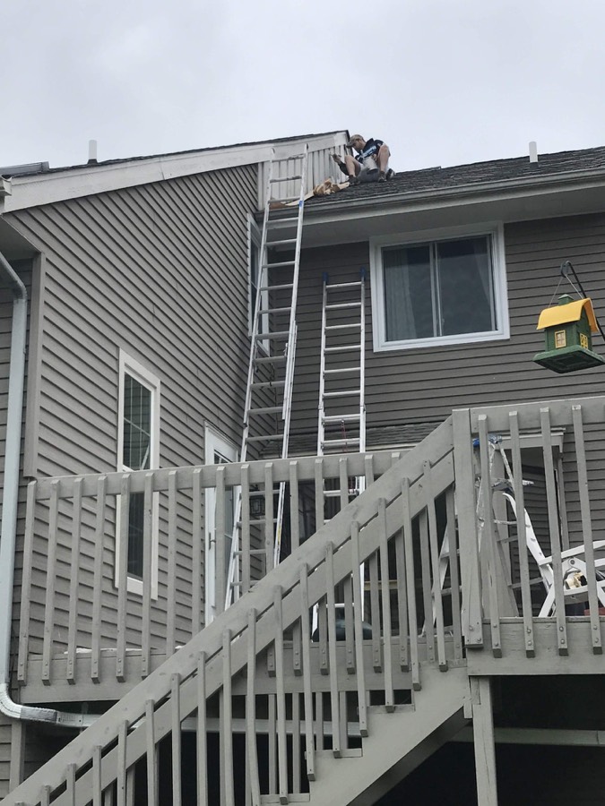 Painter working on trim along a second-story roof edge with ladders in place