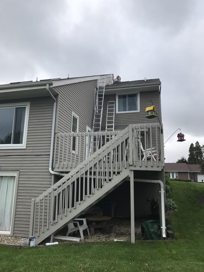 Painter working along the roofline of a two-story gray home