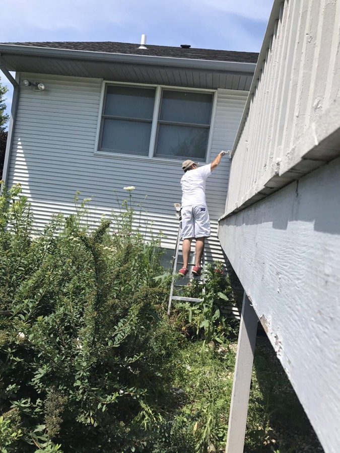 Painter on a ladder repainting the fascia and trim along a roofline
