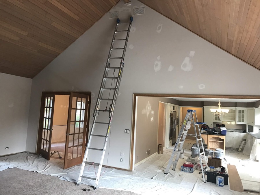 Great room mid-remodel with ladders and drywall patching, opening into the kitchen